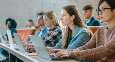 Large Group of Multi Ethnic Students Working on the Laptops while Listening to a Lecture in the Modern Classroom. Bright Young People Study at University.