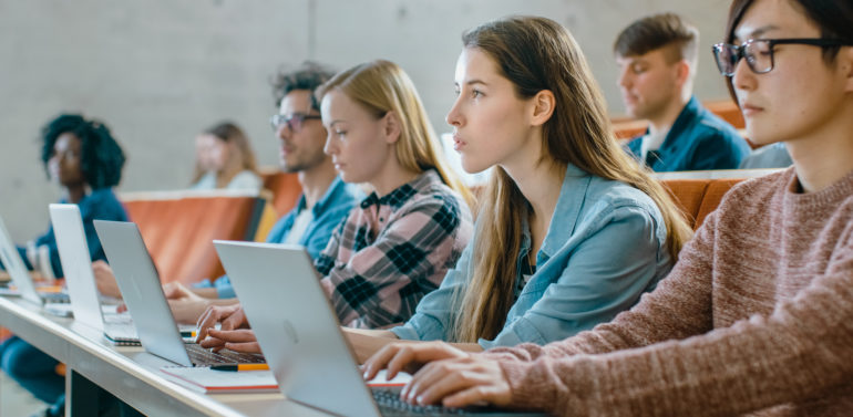 Large Group of Multi Ethnic Students Working on the Laptops while Listening to a Lecture in the Modern Classroom. Bright Young People Study at University.